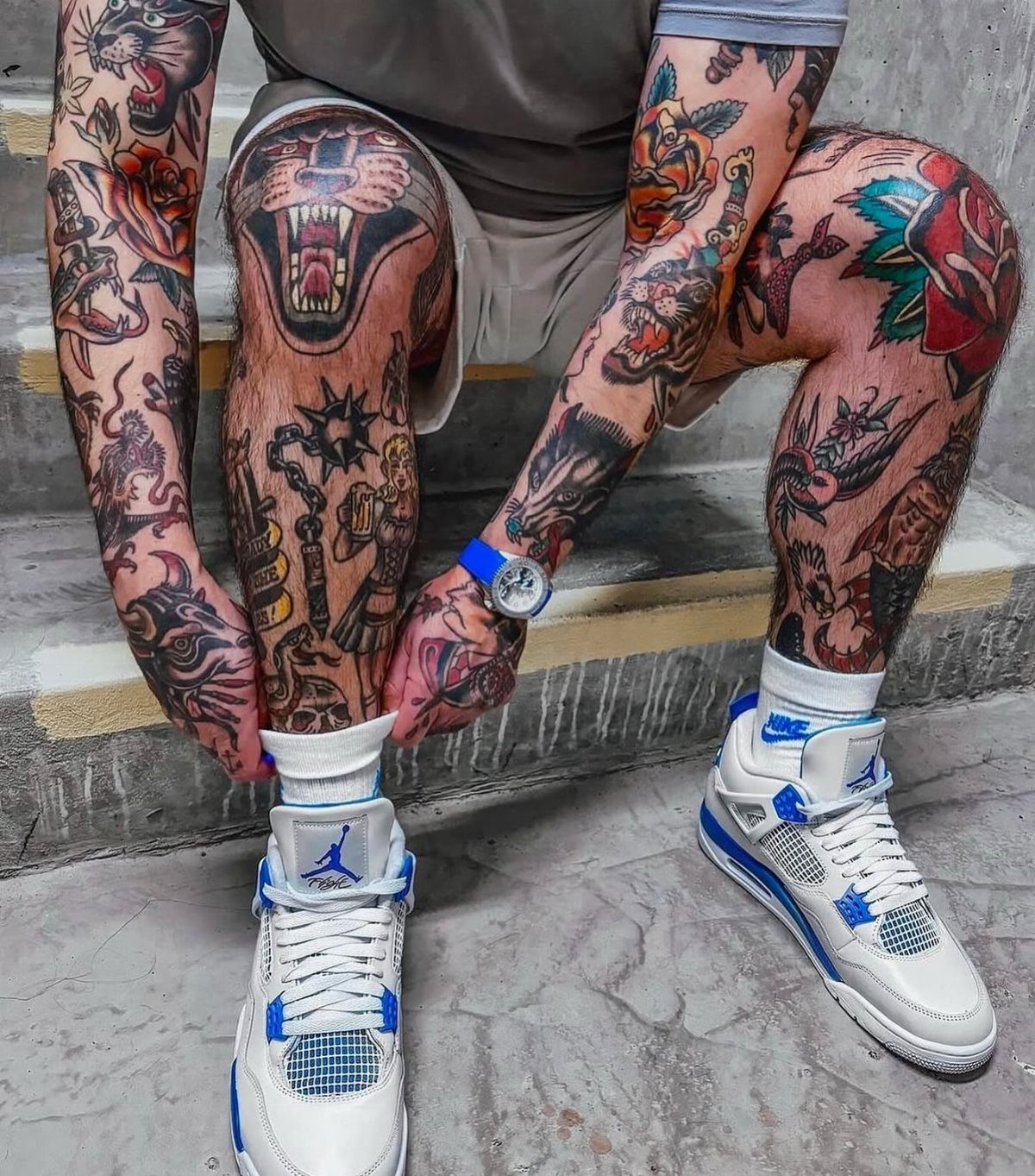 A person sitting on steps with extensive American traditional tattoos on their arms and legs.