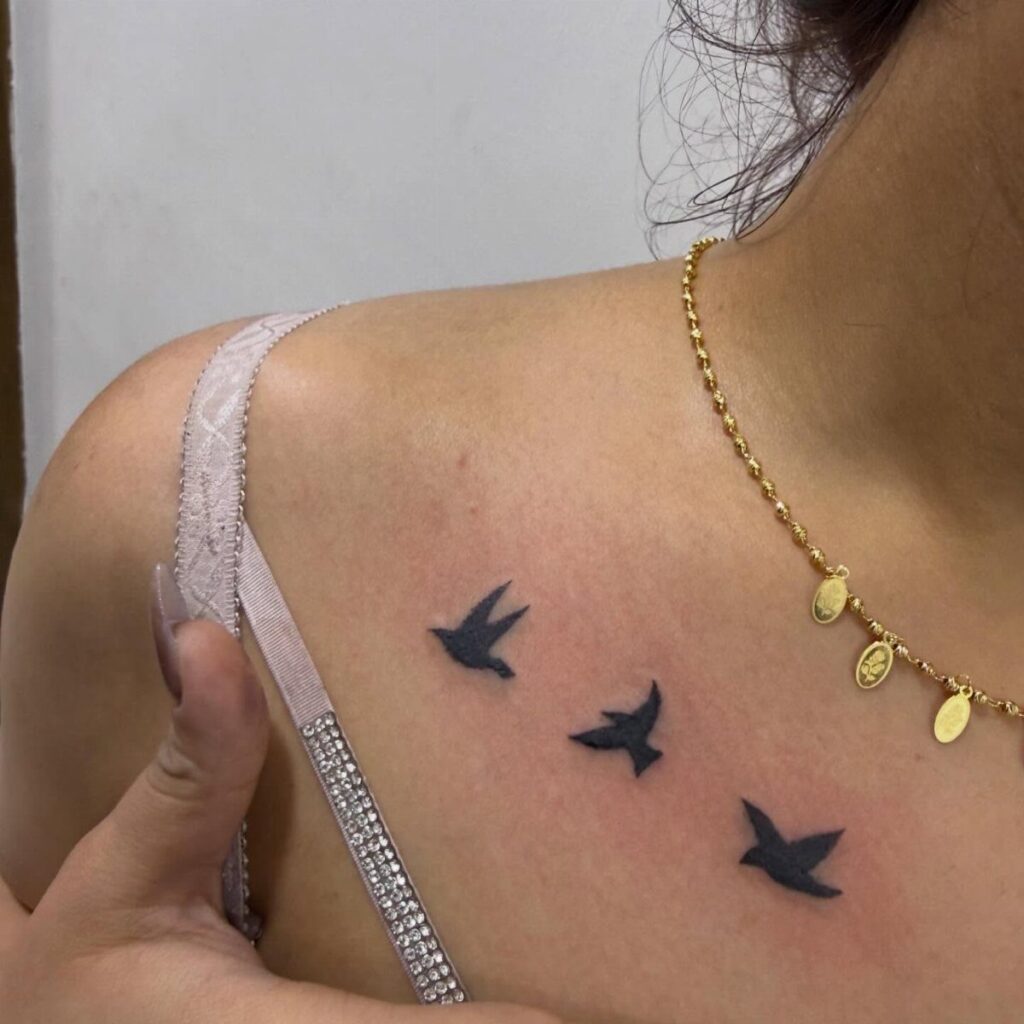 Three small black silhouette bird tattoos flying along a person's collarbone area.