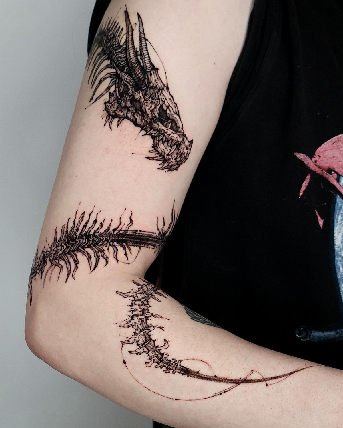 A black ink dragon skull and spine tattoo on a person's arm.