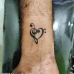 A black ink tattoo of a treble clef combined with a heart shape on a wrist.