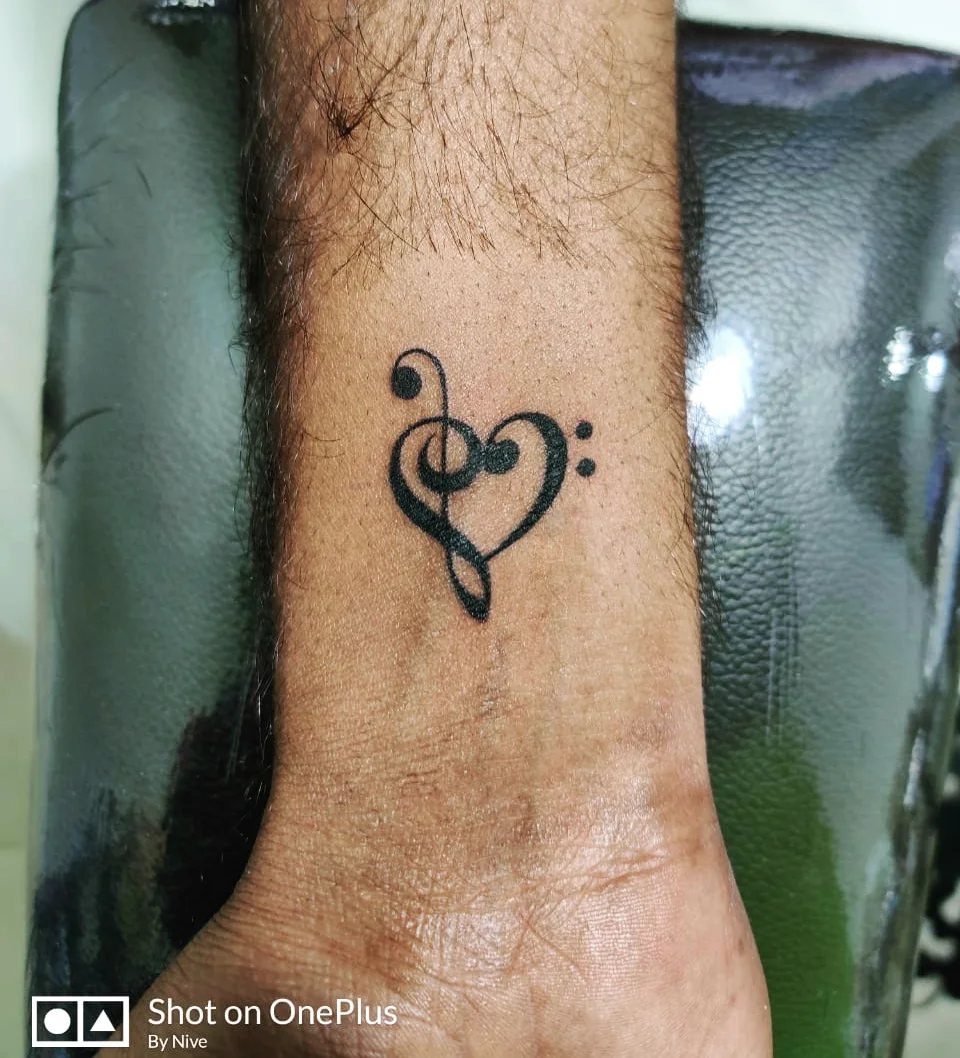 A black ink tattoo of a treble clef combined with a heart shape on a wrist.