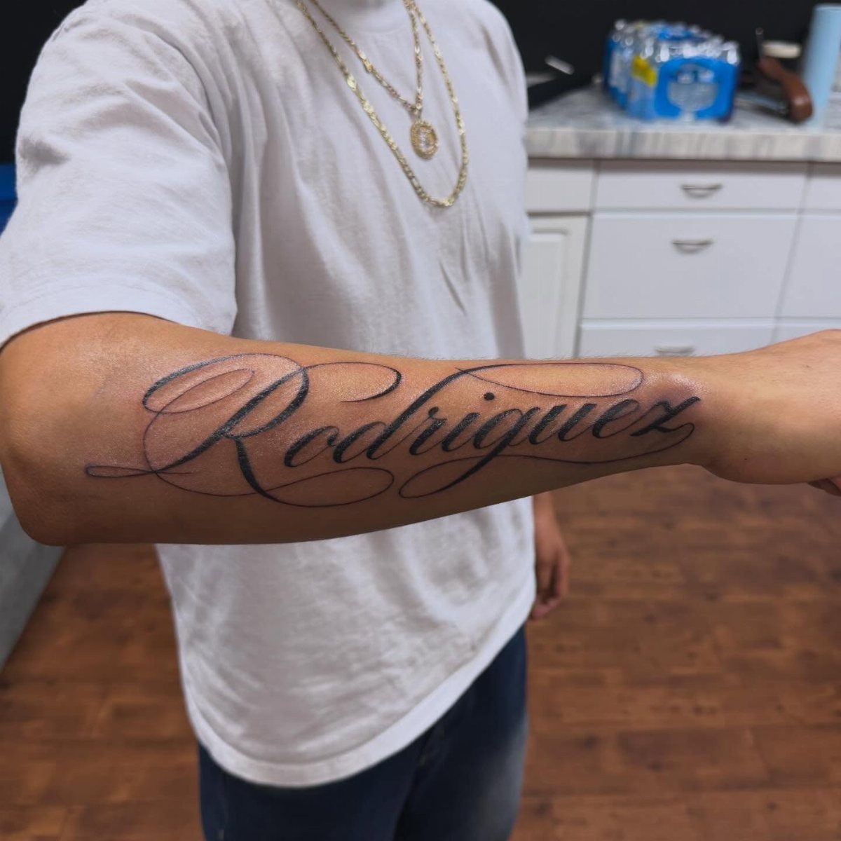 A person's forearm displaying a large black cursive tattoo of the name Rodriguez.