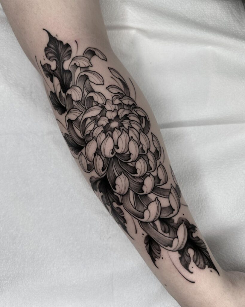 A large black and grey chrysanthemum flower tattoo covering a person's forearm.