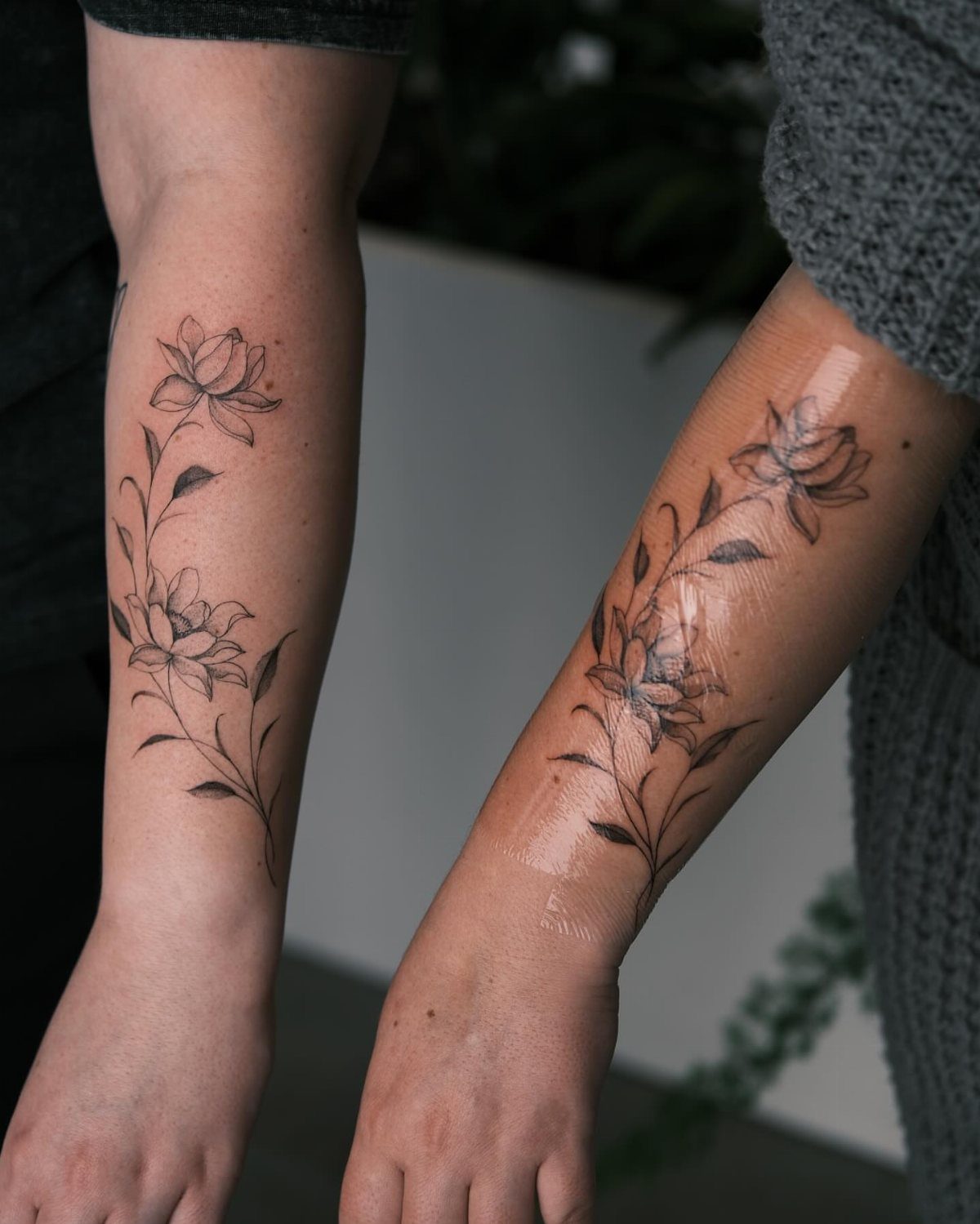Two arms displaying black ink lotus flower vine tattoos with delicate leaves and floral patterns.
