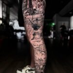 A detailed black and grey tattoo on a leg depicting a lighthouse, ship, and octopus.