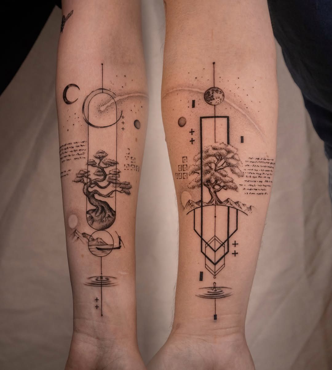 Two forearms displaying matching black ink geometric tattoos of moons and bonsai trees.