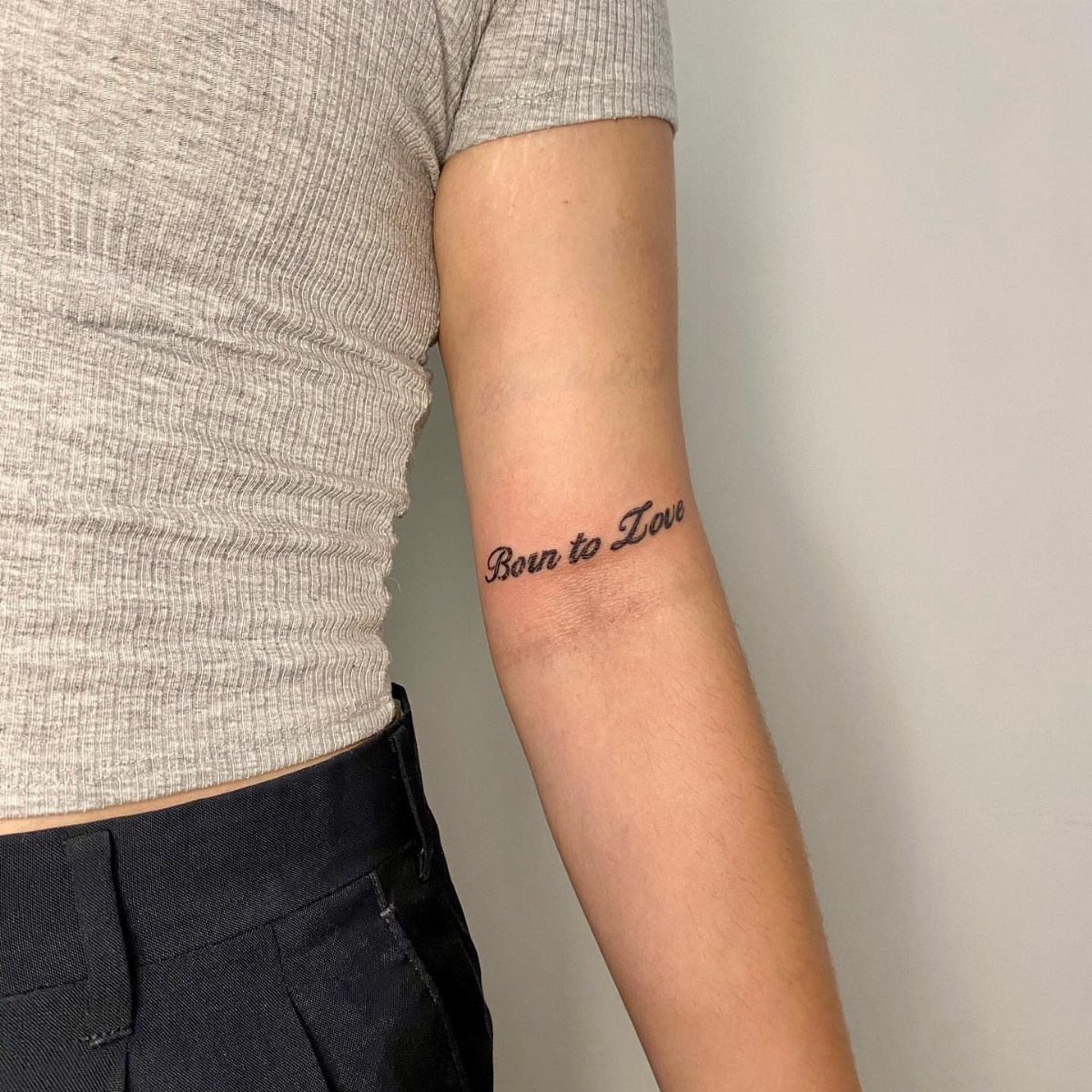 A person's forearm displaying a black script tattoo that reads Born to Love.