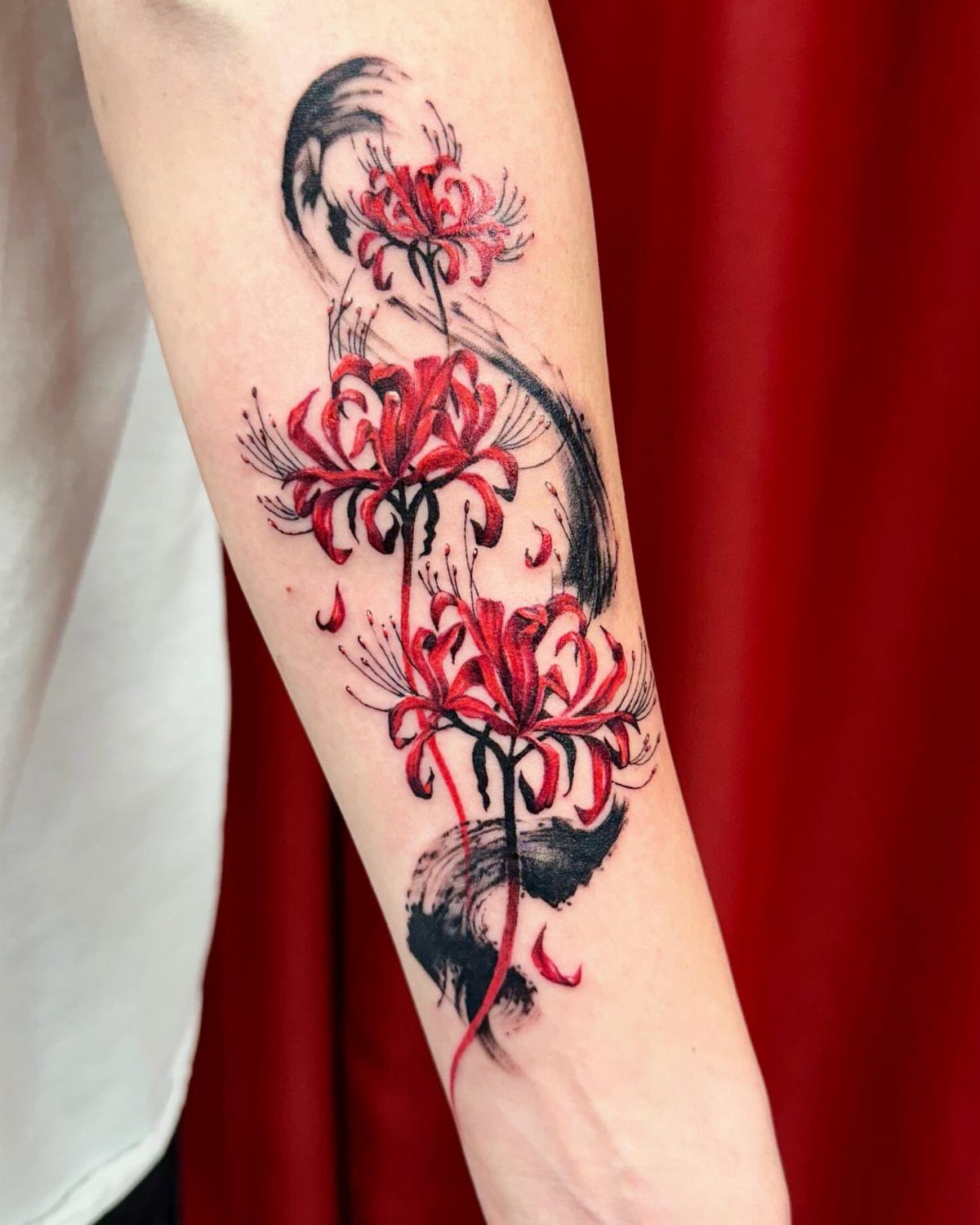 Red spider lily tattoo with black ink brushstrokes on a person's forearm.