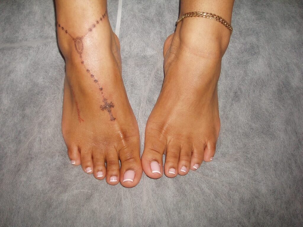 A person's feet showing a rosary tattoo with beads and a cross on the left foot.