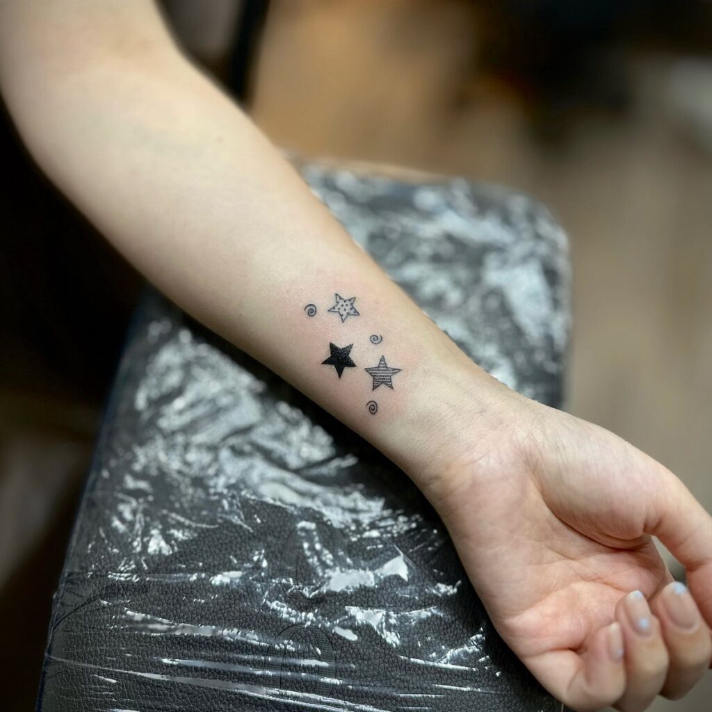 Small black and outlined star tattoos on a person's inner forearm.