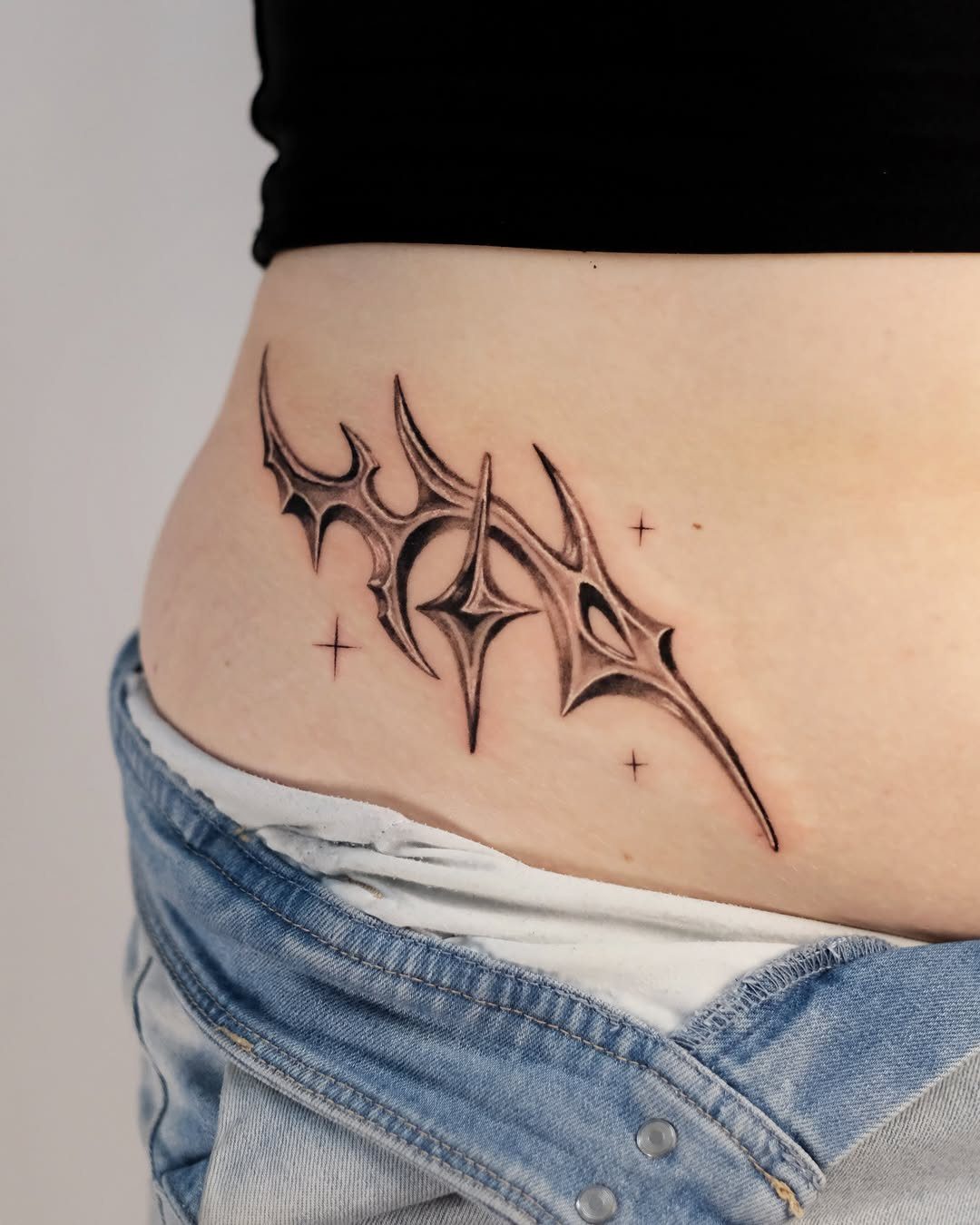 A black tribal tattoo with star accents on a person's waist above denim jeans.