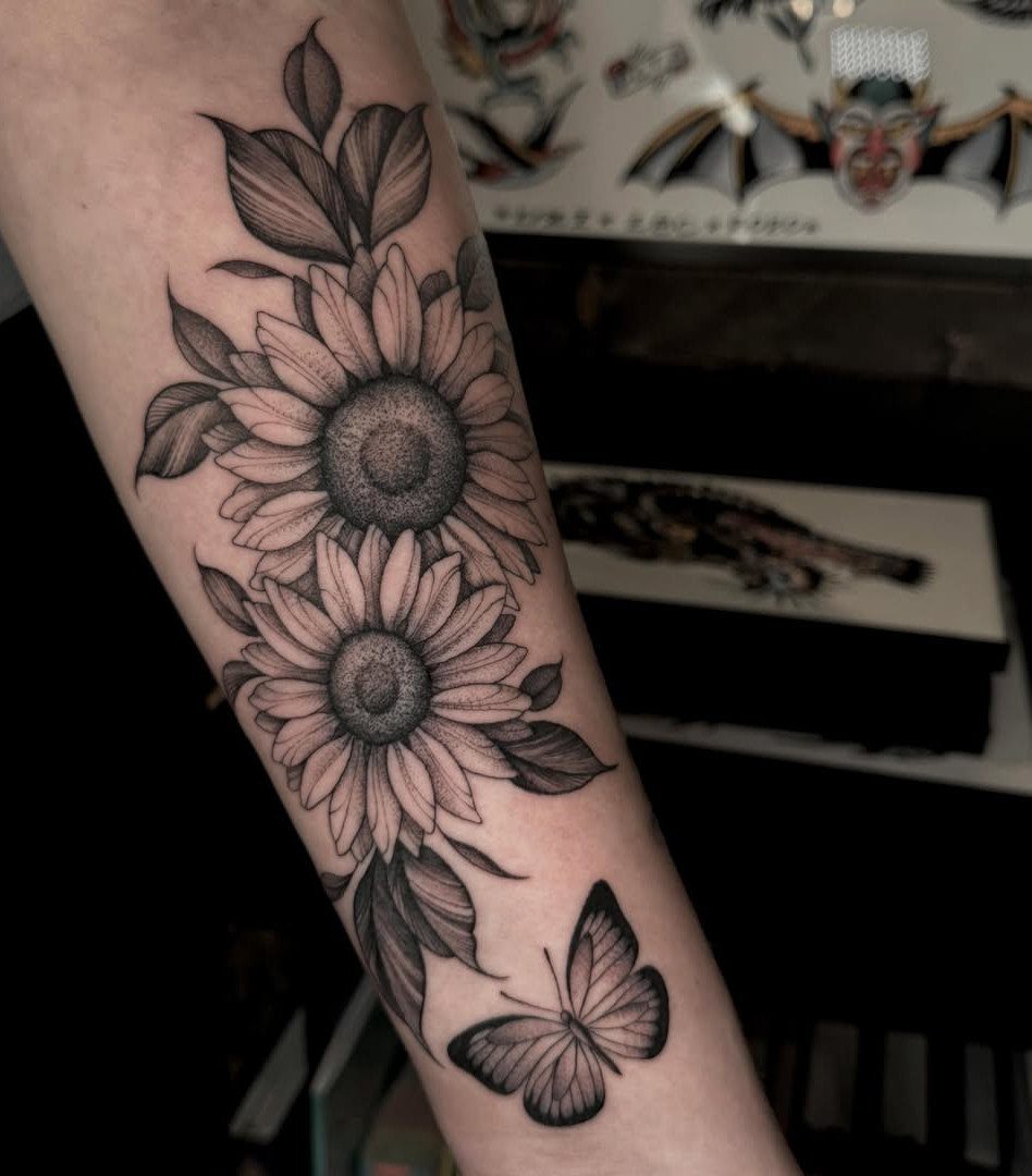 Two large sunflower tattoos with leaves and a butterfly on a person's forearm.