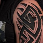 A large black and grey tribal pattern tattoo on a person's shoulder and upper arm.