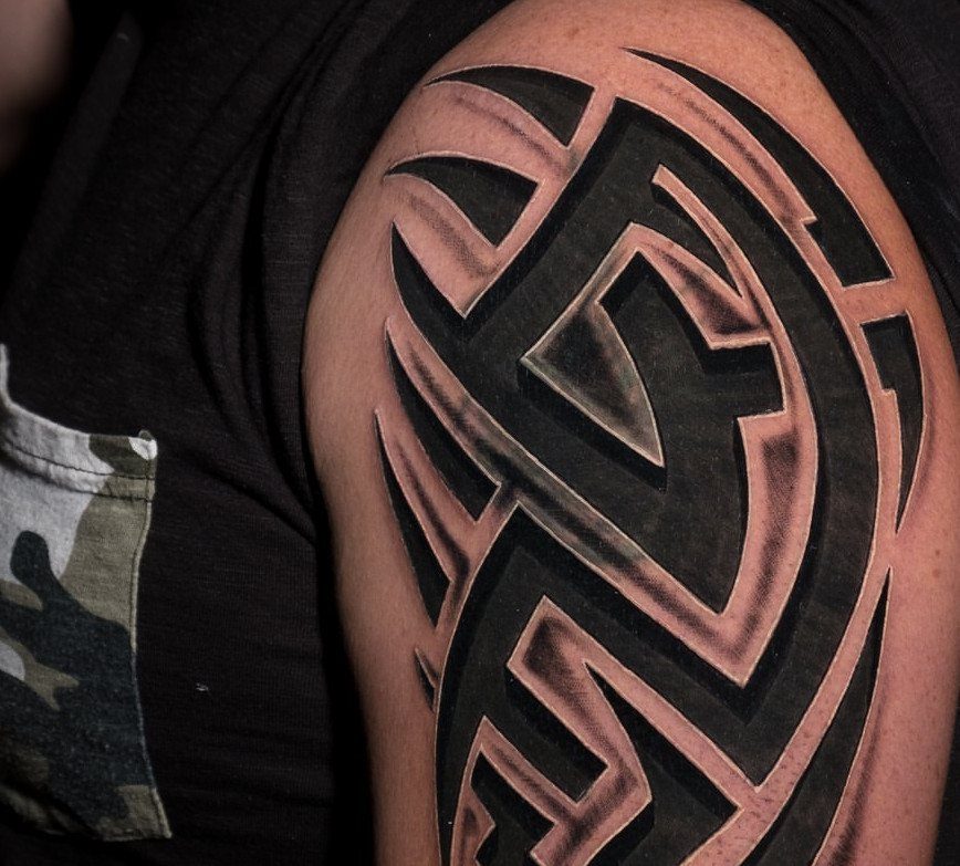 A large black and grey tribal pattern tattoo on a person's shoulder and upper arm.
