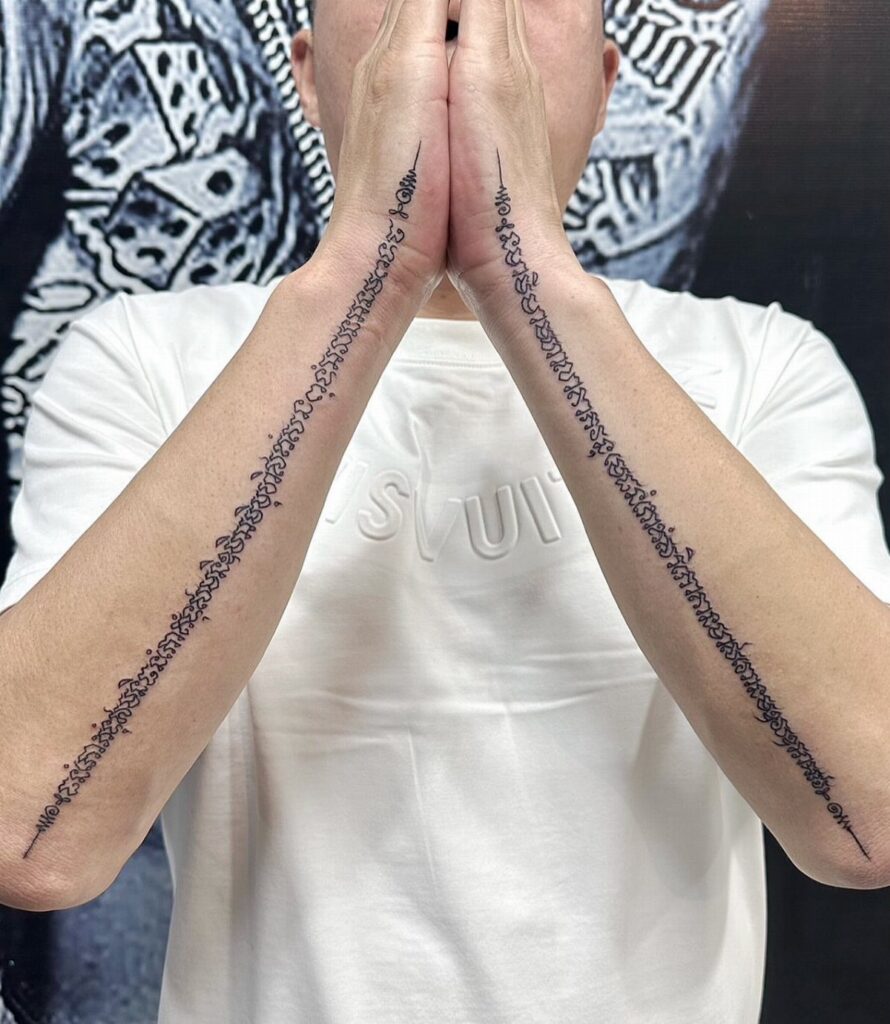 A person displaying long black script tattoos running down the length of both forearms.