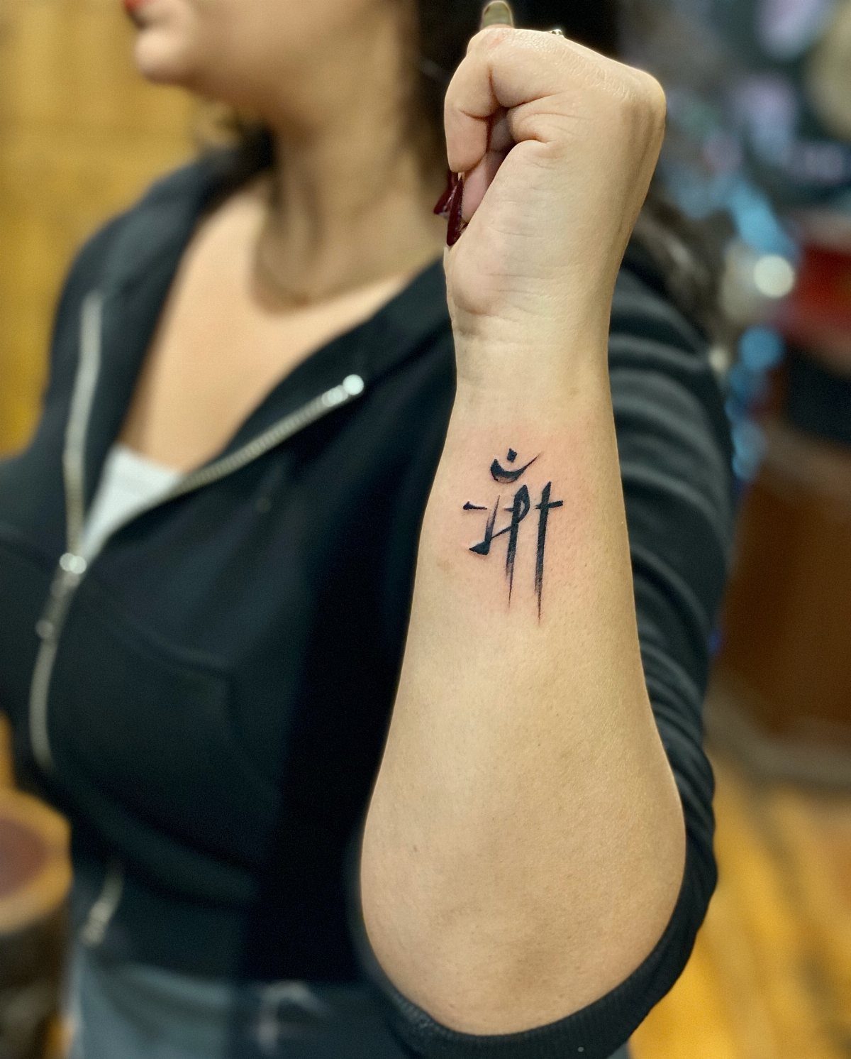 A small black minimalist line art tattoo on a person's inner forearm.