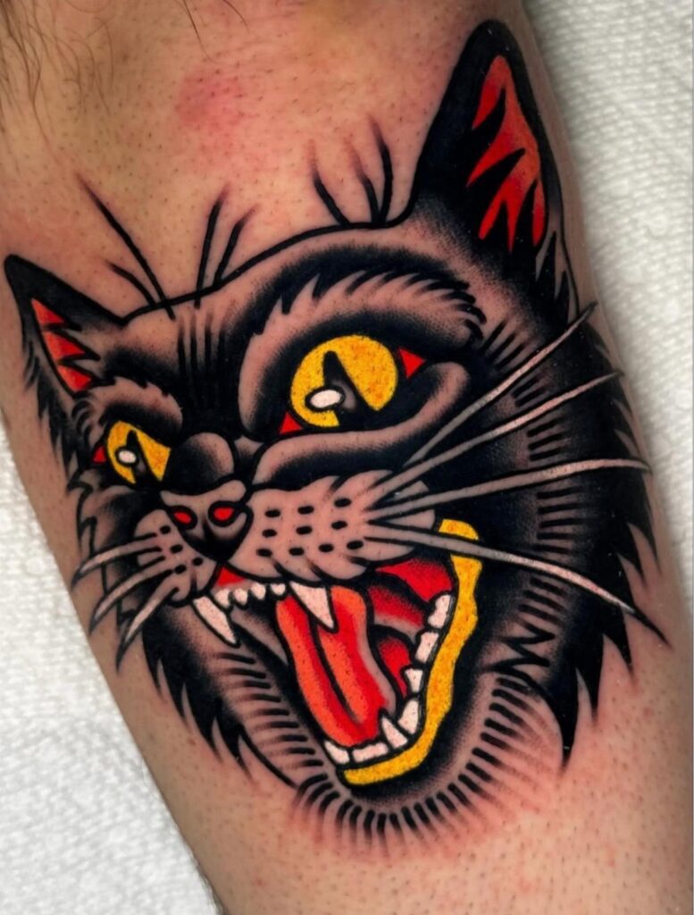 A traditional black cat tattoo with yellow eyes and sharp teeth on human skin.