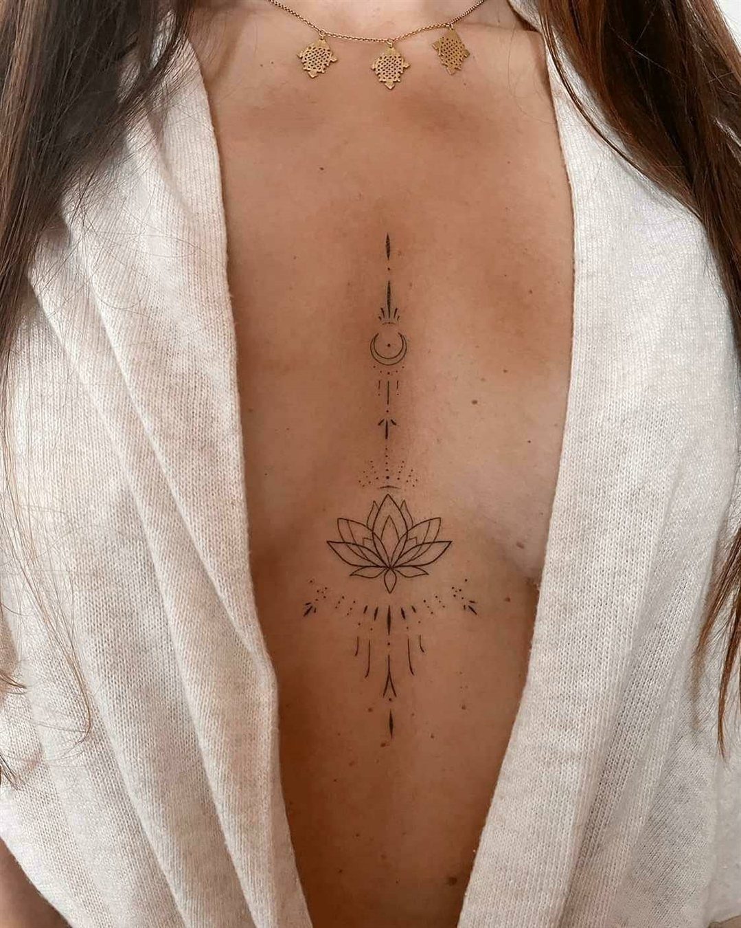 A fine-line lotus and moon tattoo centered on a woman's sternum.